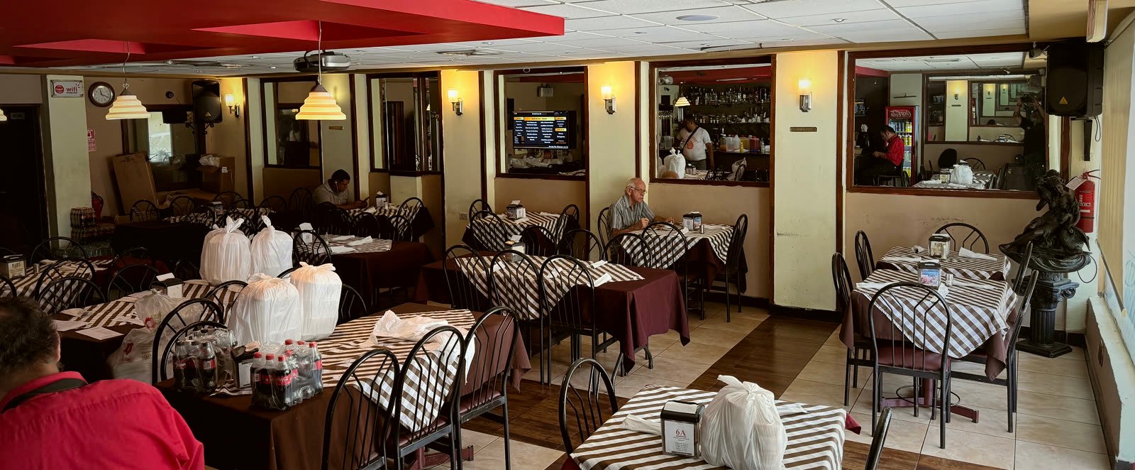 Salón de Pekrys en pleno almuerzo: mesas puestas, clientes comiendo y los pedidos de delivery listos para salir